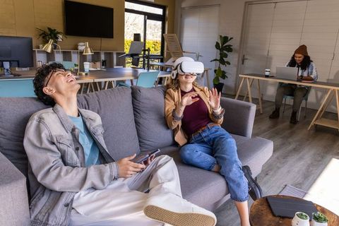 Young diverse coworkers using vr headset and smartphone in modern sunlit coworking lounge