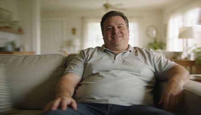 Middle-aged man relaxing on couch in sunlit living room wearing casual polo shirt
