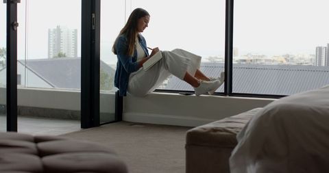 Woman writing notebook on window ledge with urban view