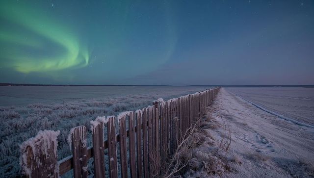Frosted picket fence stretching across frozen plain under northern lights