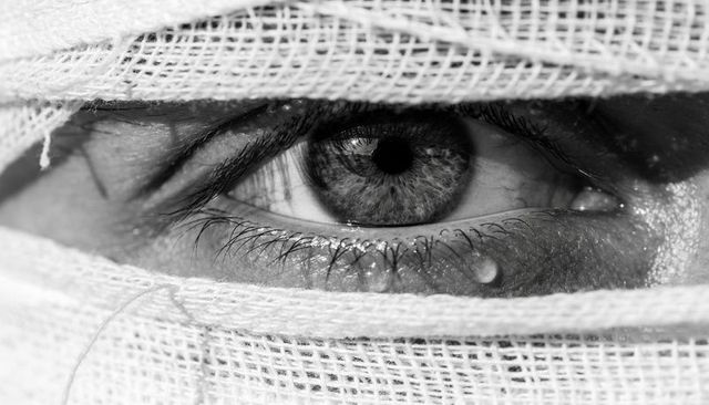 Focusing single gauze-wrapped eye revealing detailed iris and tear droplet in monochrome