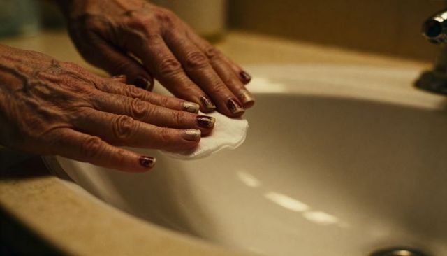 Senior woman removing maroon metallic nail polish at vanity sink