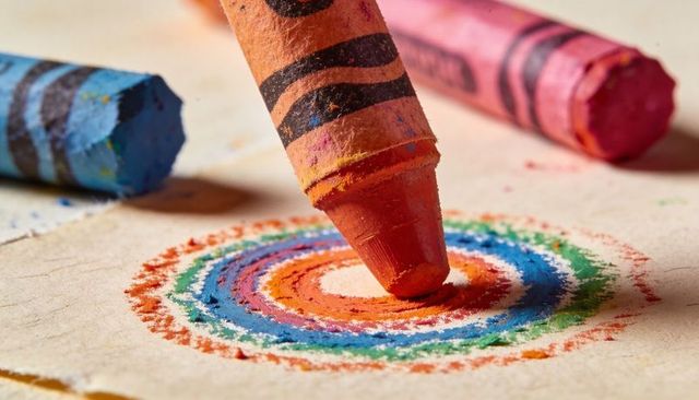 Macro orange crayon drawing colorful concentric rings on textured beige paper