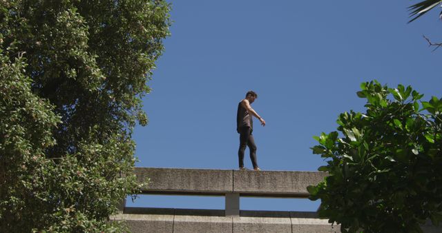 Young man walking along building ledge with clear blue sky - Download Free Stock Images Pikwizard.com