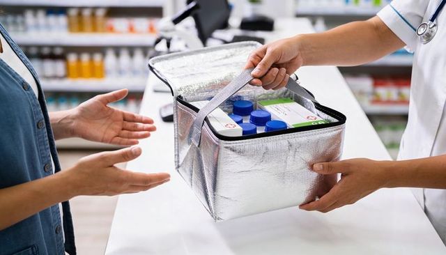 Pharmacist handing insulated medication bag with prescriptions at pharmacy counter