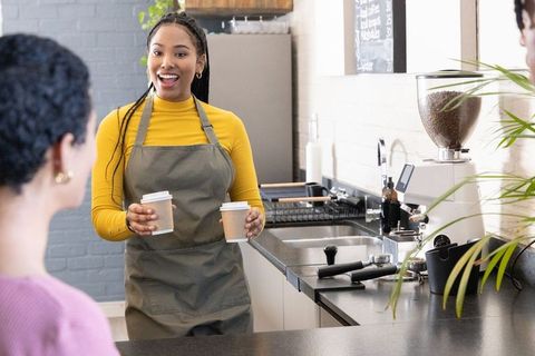 African american barista handing two takeaway coffees with warm smile in cozy cafe