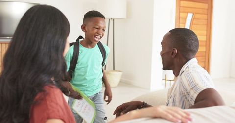 Smiling schoolboy showing drawing to parents at home with backpack and playful energy
