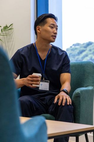 Asian male healthcare professional taking coffee break in staff lounge wearing navy scrubs