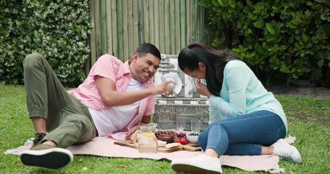 Young couple enjoying outdoor picnic with snacks and laughter