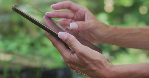 Close-up of Hands Using Tablet in Lush Garden Outdoors