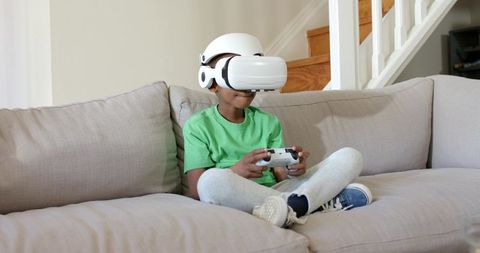Boy playing virtual reality game on couch wearing white VR headset and controller