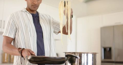 Man lifting fresh pasta with tongs from pot into skillet in bright modern kitchen