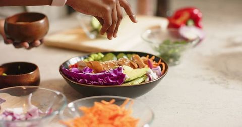 African american woman sprinkling sesame seeds on colorful healthy grain bowl at kitchen counter