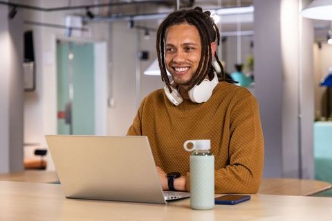 African American man smiling while working on laptop in modern coworking space