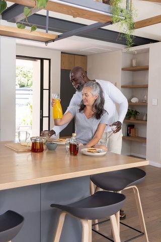 Senior couple pouring orange juice and serving toast at modern bright cozy kitchen island