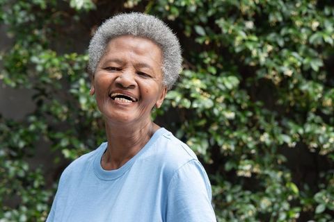 Senior african woman smiling in sunlit garden wearing blue tee and stud earrings portrait