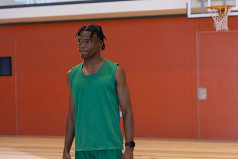 African american basketball player standing on indoor court in green jersey and shorts