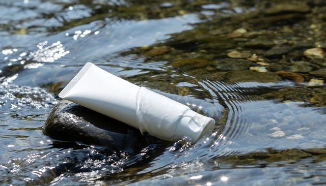 White Cosmetic Tube Resting on River Rock with Sunlit Water Ripples and Pebble Creek