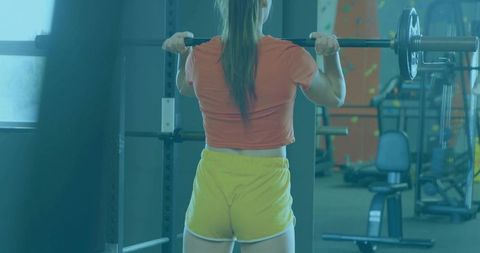 Woman performing barbell squat in gym for strength training