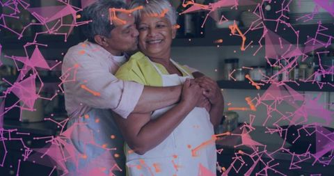 Senior couple embracing and kissing in kitchen wearing apron with warm geometric overlay