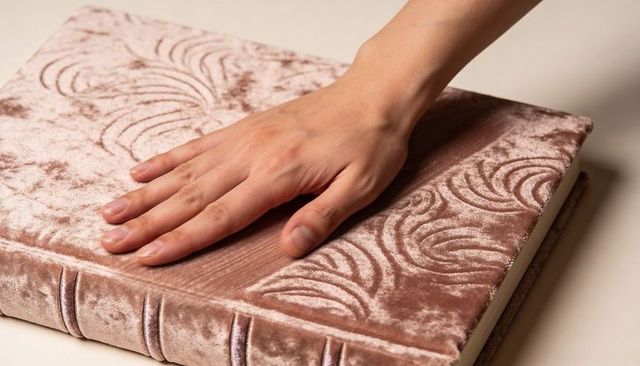 Hand resting on embossed velvet journal with dusty rose swirl texture closeup