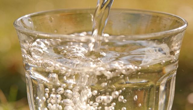 Sunlit water pouring into faceted glass creating rising bubbles and sparkling reflections