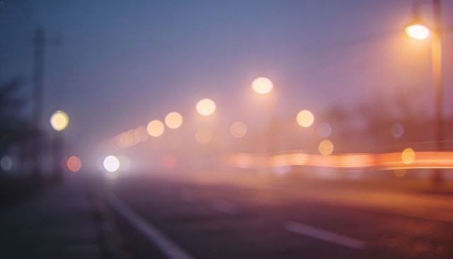 Foggy urban avenue with glowing streetlight bokeh and vehicle light trails at night