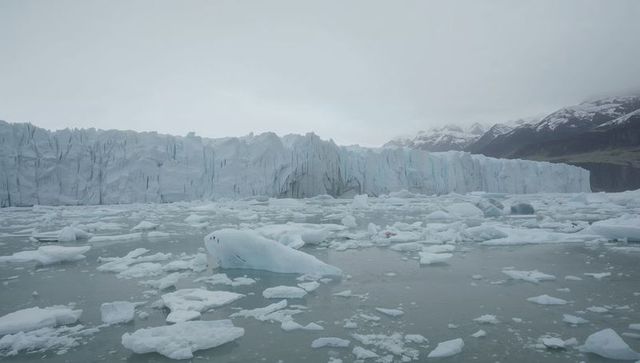 Glacier terminus forming jagged ice wall with floating icebergs in arctic fjord
