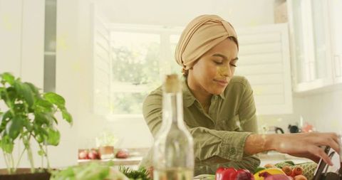 Woman in headwrap preparing fresh fruit and vegetables on sunny kitchen counter