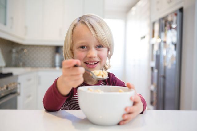 Young boy enjoying breakfast in a modern kitchen. Ideal for use in family lifestyle, healthy eating, and home environment promotions. Perfect for illustrating morning routines, childhood happiness, and family-oriented content.