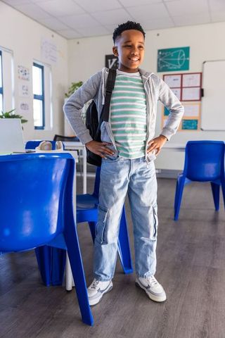 Confident african american boy standing in classroom wearing backpack and hoodie