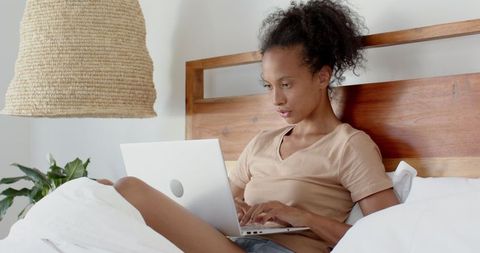 Woman remote working on laptop in cozy bedroom setting