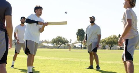 Diverse men playing cricket batting and fielding on sunny community sports field