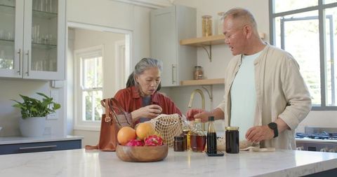 Senior couple unpacking groceries and organizing bottles at bright modern kitchen island