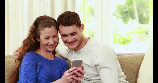 Happy couple smiling and using smartphone together on sofa - Download Free Stock Images Pikwizard.com