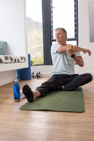 Mature man stretching on yoga mat at home promoting mobility, posture and wellness