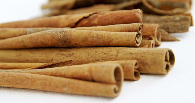 Cinnamon sticks are piled together against a white background, with copy space. Their warm, earthy tones and texture highlight the natural qualities of this popular spice.
