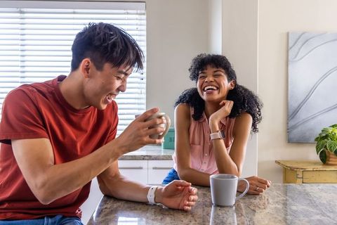 Laughing young adults sharing coffee and conversation at sunlit kitchen island