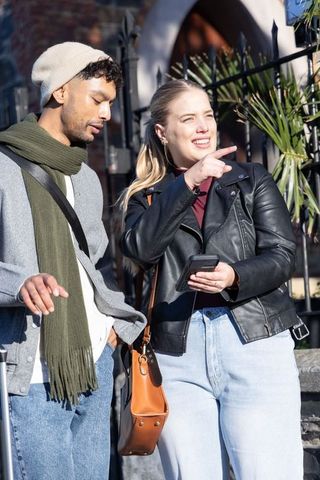 Young couple navigating city streets pointing at landmark while using smartphone outdoors
