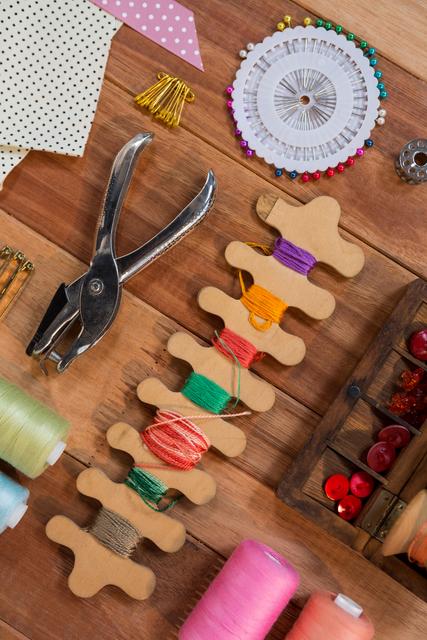 This image showcases a variety of sewing tools and supplies arranged on a wooden table. It includes thread spools, scissors, pins, buttons, and fabric pieces, making it ideal for use in articles or advertisements related to sewing, crafting, DIY projects, and handmade goods. Perfect for illustrating blog posts, tutorials, or promotional materials for sewing workshops and craft stores.