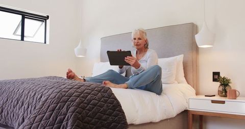 Senior Woman Relaxing with Tablet in Bright Minimalist Bedroom