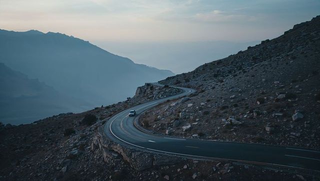 Sedan navigating winding alpine mountain pass at dusk with serpentine asphalt curves