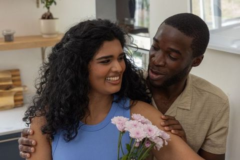 Diverse couple sharing warm moment holding pale pink bouquet in cozy kitchen interior