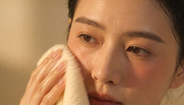 Asian woman pressing soft towel against glowing dewy skin after cleansing