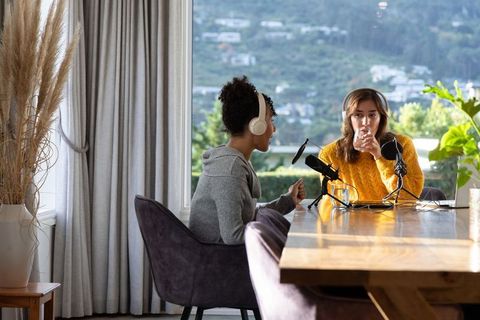 Multiracial women cohosting cozy at-home podcast interview with microphones headphones natural light