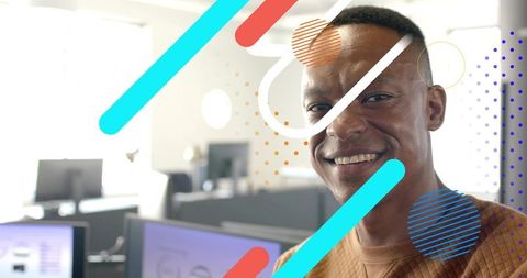 Smiling man wearing sweater facing camera in modern open-plan office with graphic overlays