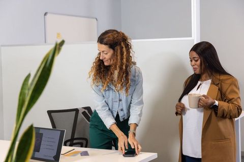 Diverse female coworkers collaborating in modern office with laptop, coffee and smartphone