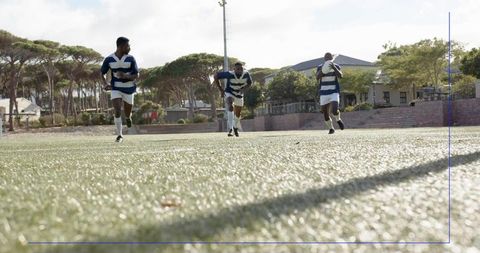 Three rugby players sprinting on artificial turf for speed and teamwork in sunlight