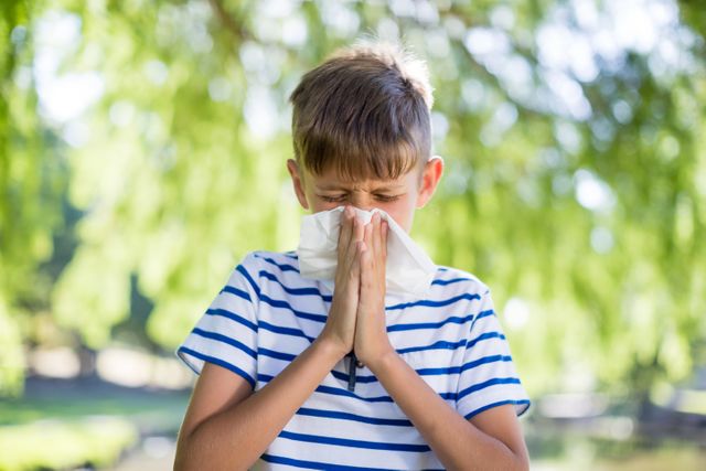 Boy wiping his nose while sneezing in a park