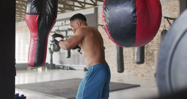 This visual shows a shirtless man in blue shorts training with boxing equipment in a gym. Perfect for visuals related to fitness training, boxing, sports promotion, and gym advertisements.
